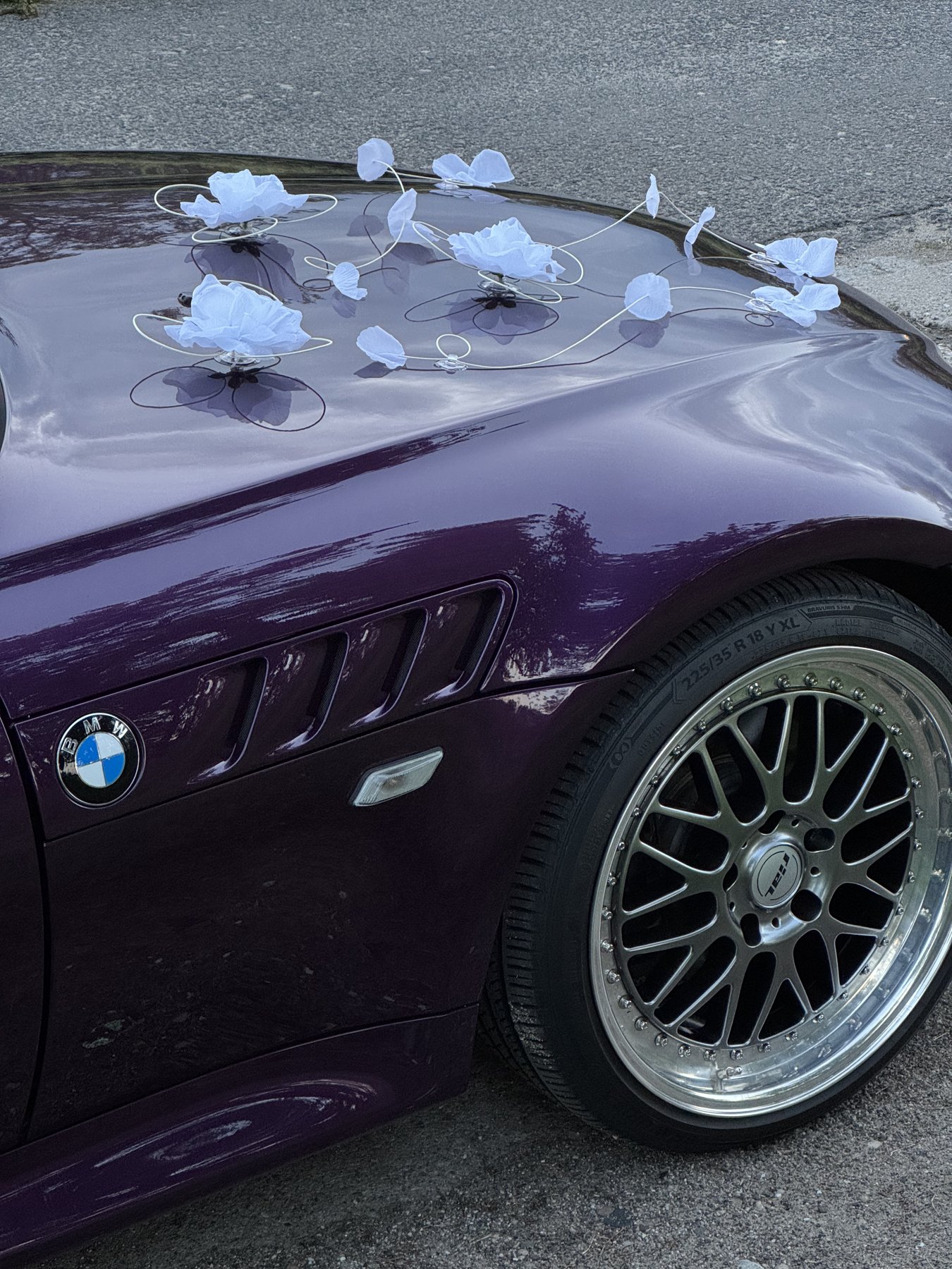 Detale dekoracji ślubnej na masce fioletowego BMW Z3 — kwiaty i wstążki